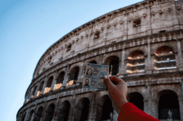 mano con documento italiano al frente del coliseo en Roma. requisitos ciudadania italiana
