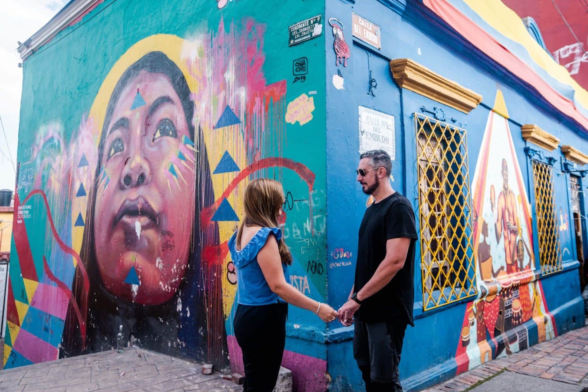 Pareja agarrandose las manos en una esquina con arte urbano del barrio de La Candelaria en Bogota, Colombia