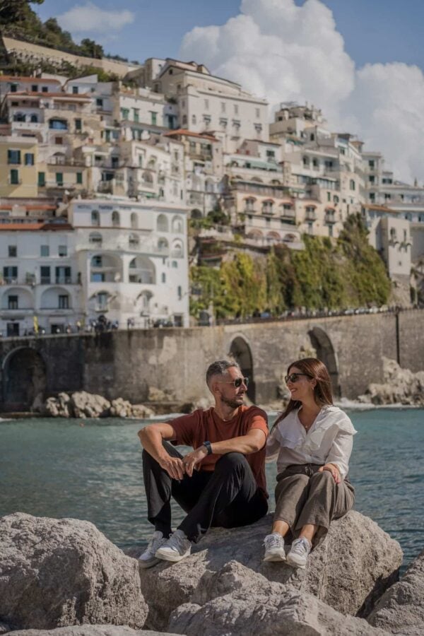 Pareja sentada sobre las rocas de la playa de Amalfi